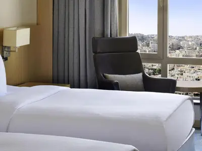 a hotel room with a bed and a chair and a window at Mövenpick Hotel Amman in Amman