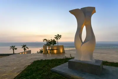 a statue in front of the ocean at sunset at Kempinski Hotel Ishtar Dead Sea in Sowayma