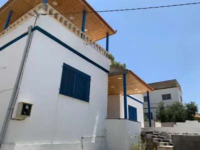 a white building with blue windows and a wooden roof at Gedara Guesthouse: enjoy unforgettable scenes in Um Qeis