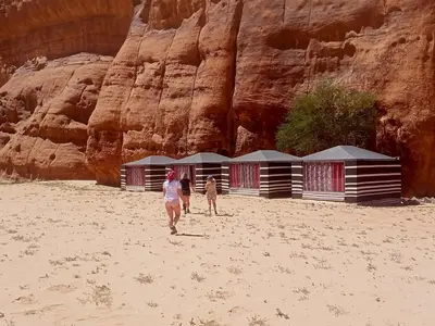 a group of people walking on the sand in front of buildings at Shahrazad desert, Wadi Rum in Wadi Rum