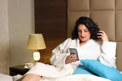 a woman sitting in a bed looking at her cell phone at The Castle Hotel in Amman