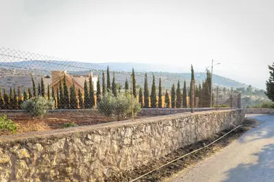 a stone retaining wall with trees and a fence at Sultana Farm - Private Pool Villa near Amman in Bayyūḑah