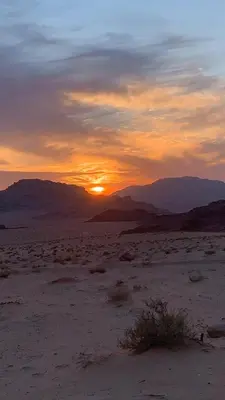 a sunset in the desert with mountains in the background at Abdullah desert trips in Wadi Rum
