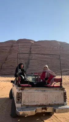 two people sitting in the back of a truck in the desert at Abdullah desert trips in Wadi Rum