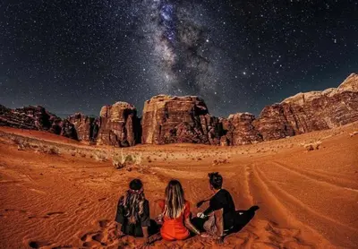 a group of people sitting in the desert under the stars at Abdullah desert trips in Wadi Rum