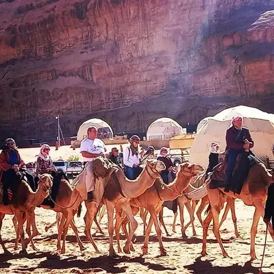 a group of people riding on camels in the desert at orbit camp 2 in Wadi Rum