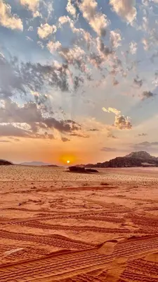 a sunset in the desert with the sun setting at Wadi rum Moon Iight Camp in Wadi Rum