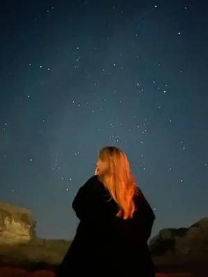 a woman with red hair walking under a night sky at Bubble RumCamp in Wadi Rum