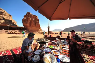 two men sitting at a table with food on the beach at SunCity Camp in Wadi Rum