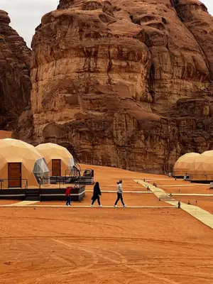 three people walking down a dirt road in front of a mountain at Montana Camp wadi rum in Wadi Rum