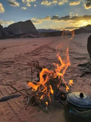 a campfire on the beach with the sunset in the background at Wadi Rum albasli in Wadi Rum