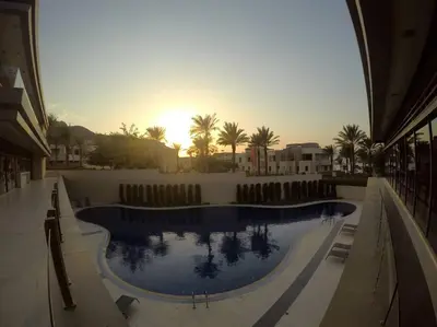 a large swimming pool with the sun setting in the background at Rental unit in RAHA village compound, special view in Aqaba