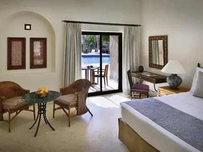 a hotel room with a bed and a table and chairs at Mövenpick Resort & Spa Dead Sea in Sowayma