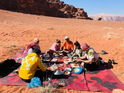 a group of people sitting around a picnic table in the desert at Wadi Rum Story Camp in Wadi Rum