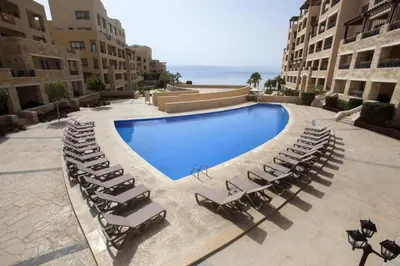 a swimming pool with lounge chairs next to a building at Comfy Stays Sea View Apartments at DeadSea Samarah Resort in Sowayma