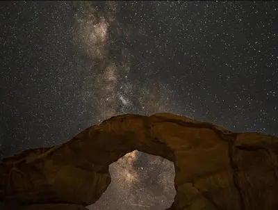 a starry night with a stone arch in the sky at rum rema camp in Wadi Rum