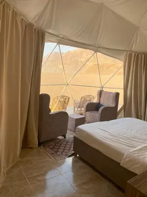 a bedroom with a bed and chairs in a tent at Qimam Al Sarab Camp Wadi Rum in Wadi Rum