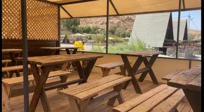 a group of picnic tables and benches under a tent at Wadi Al-Hassa camp in Khawkhah