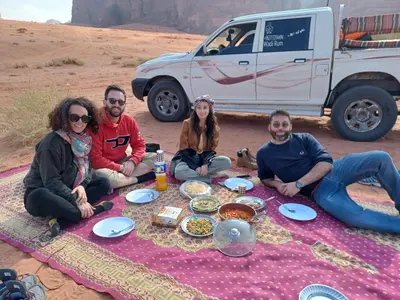 a group of people sitting around a picnic blanket at falling Stars Camp in Wadi Rum