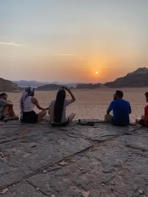 a group of people sitting on the beach watching the sunset at Sandy Camp Wadi Rum in Wadi Rum