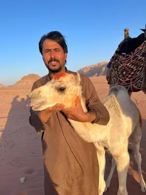 a man standing in the desert holding a camel at Wadi Rum Magic Camp in Wadi Rum