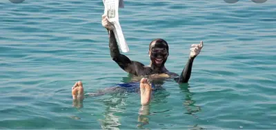 a man in the water holding up a object at Dead sea 2 bedroom apartment in Astana ,swemeh Jordan in Sowayma