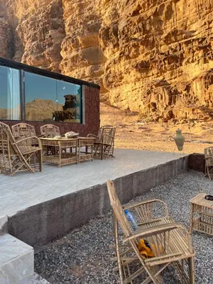 a patio with chairs and tables in front of a cliff at Adam Bedouin camp in Wadi Rum