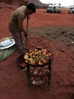 a man cooking food on a grill in the desert at Wadi Rum Desert Stars in Wadi Rum