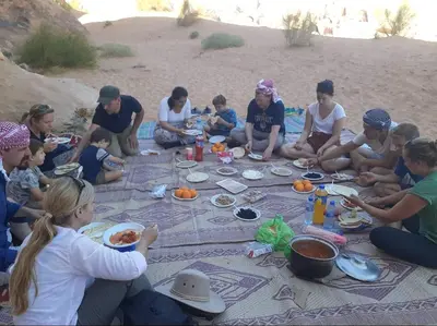 a group of people sitting on the beach eating food at Wadi Rum Desert Stars in Wadi Rum