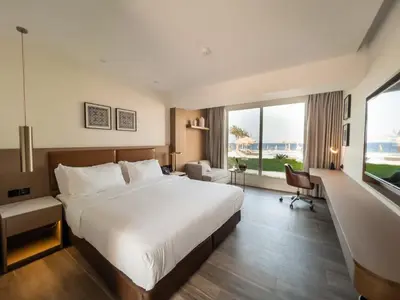 a hotel room with a large bed and a large window at Luxotel Aqaba Beach Resort & Spa Only 15 years plus in Aqaba