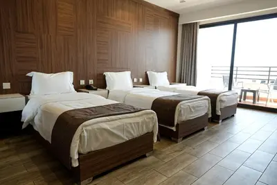 a hotel room with three beds and a large window at Luciana Hotel by FHM in Aqaba