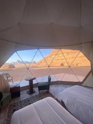 a tent with two beds and a table and a chair at Aun Wadi Rum Camp in Wadi Rum