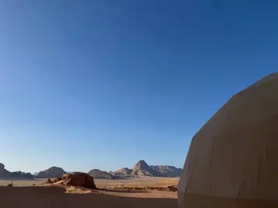 a camel in the desert with mountains in the background at Aun Wadi Rum Camp in Wadi Rum