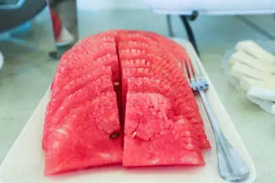 a slice of watermelon on a plate with a fork at Khuttar Apartment in Amman