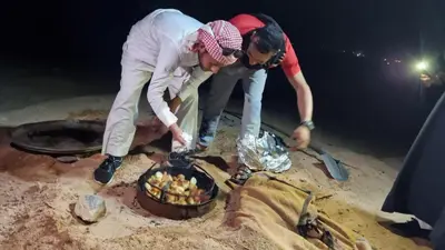 two people standing around a fire in the sand at The sunset of Wadi Rum in Wadi Rum