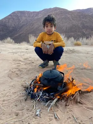 a young boy sitting next to a camp fire at Bedouin Desert Cave in Wadi Rum