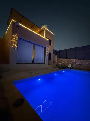 a swimming pool in front of a house at night at Lionden jerash استراحة وشالي عرين الاسد جرش in Jerash