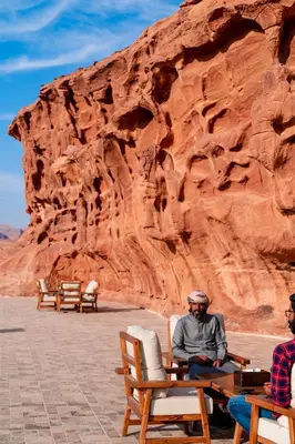 a man sitting on a bench in front of a mountain at The Villas - Bedouin Boutique Resort in Wadi Rum