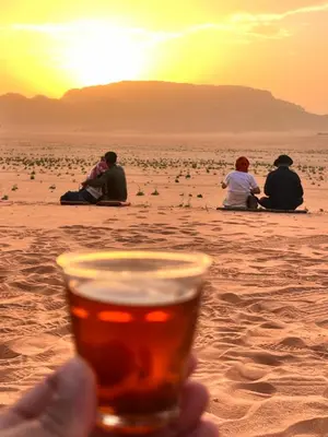 a person holding a glass of beer on the beach at Scarlet Luxury Camp Wadi Rum in Wadi Rum