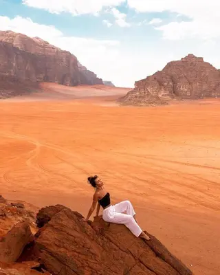 a woman sitting on a rock in the desert at Anwar Al Qamar Luxury Hotel in Wadi Rum