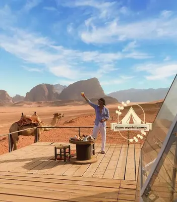 a man standing on a deck with a camel in the desert at RUM WORLD BUBBLE lUXURY CAMP in Wadi Rum