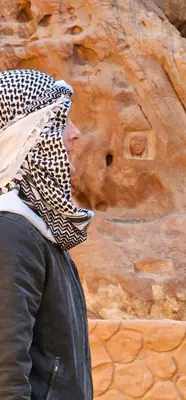 a woman wearing a scarf around her head next to a stone wall at Ammar Rum Camp and tours in Wadi Rum