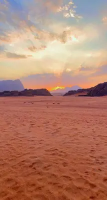 a sunset on a sandy beach with the sun in the distance at Syndebad desert camp in Wadi Rum