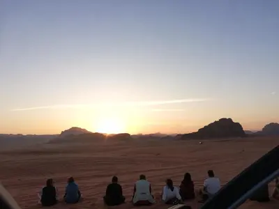 a group of people sitting in the desert watching the sunset at The calm nature of Wadi Rum in Wadi Rum