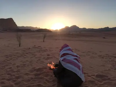 a person sitting in the desert with a bon fire at The calm nature of Wadi Rum in Wadi Rum