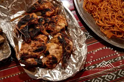 a group of chicken wrapped in foil next to a pan of noodles at Wild Oryx Camp Bubbles in Wadi Rum