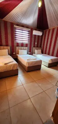 two beds in a room with a red wall at Maestro camp Wadi Rum in Wadi Rum