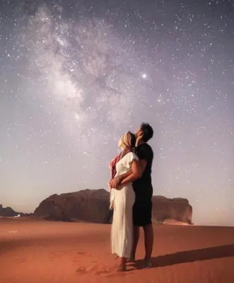a man and woman standing on the beach under the stars at Star rum in Wadi Rum
