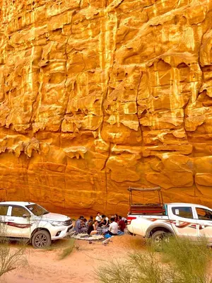a group of people standing in front of a rock wall at RUM ARJAAN lUXURY CAMP in Wadi Rum
