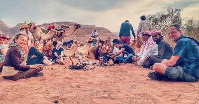 a group of people sitting in the sand with camels at Wadi Rum Red Sand Camp in Wadi Rum